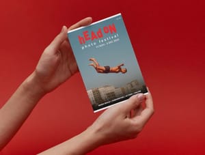 A person holding up a Pre-order: Head On Photo Festival 2023 Exhibition catalogue with a man diving into water.